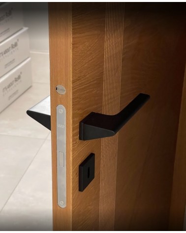 Maniglia porta nera LUPINA design montata su una porta socchiusa