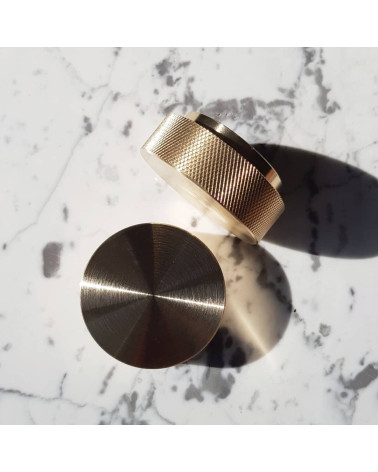 Pomello per mobile oro opaco TOVE maniglia design vista dall'alto leggermente inclinati posati su una superficie marmorizzata bi
