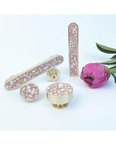 Pomello per mobile in ottone e Pink Terrazzo maniglia design disposto accanto a un fiore su sfondo bianco
