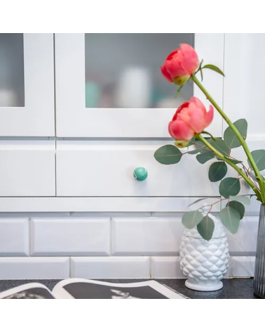 Pomello per mobile in legno di faggio verde intenso maniglia design montata su un mobile con delle rose sopra
